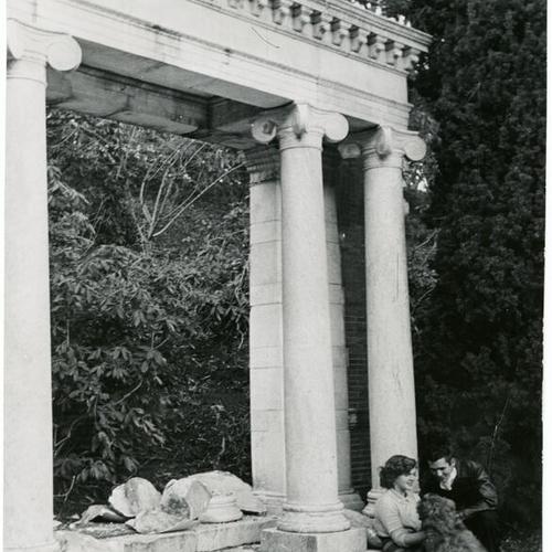 [Woman and a man with a dog in front of the Portals of the Past monument in Golden Gate Park]