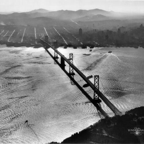 [Aerial view of suspension section of Bay Bridge with San Francisco in background]