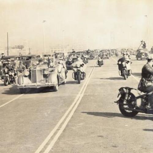 [Automobiles carrying dignitaries and officials led by motorcycle patrol of the bridge, driving across the San Francisco-Oakland Bay Bridge as part of opening ceremony for the bridge"