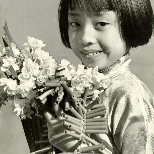 [Chinese-American girl holding flowers and fire crackers on New Years Day]