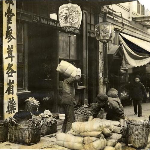 [Workers carrying merchandise outside of a store in Chinatown]