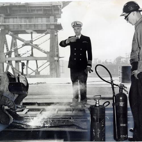 [Fire Guard Airman D. L. Ellis watching over a welding operation at  San Francisco naval shipyard]