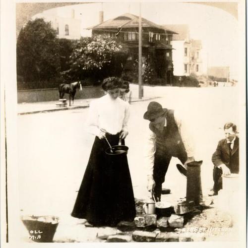 [Three people preparing a meal on an unidentified street]