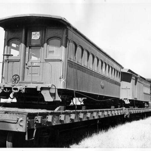 [Old train cars from the Nevada Central Railroad being transported by train for use in Railroad Museum]