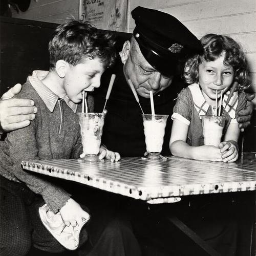 [Officer Gus Wuth with youngsters Antony Van Fleet? and Shirley Chalfant enjoying a milkshake]