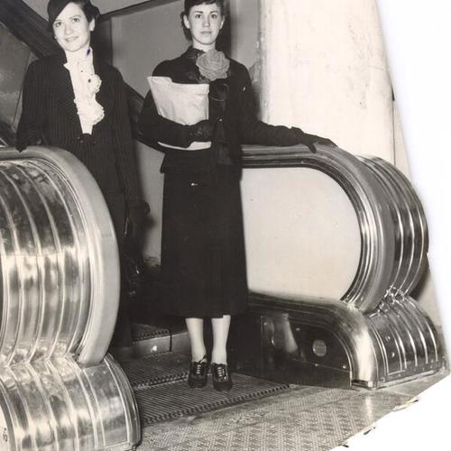 [Two women riding an escalator at the Emporium]