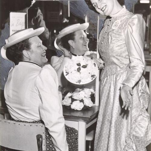 [J. C. Penney employees Georgia Ratlif and Jean Retel dressing up in preparation for a "horseless carriage parade" to mark the stores 56th anniversary]