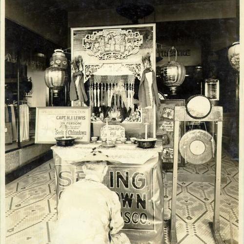 [Unidentified man kneeling in front of an altar in the lobby of a theater featuring Captain H. J. Lewis' show "Seeing Chinatown San Francisco"]