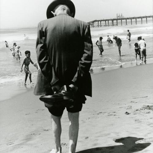 [Man walking barefoot and children playing on Ocean Beach]