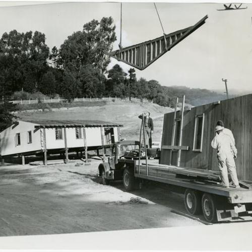[Construction workers on flatbed truck with prefabricated house]