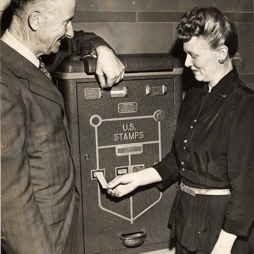 [J.J. McNaughton and Mrs. Walter Hannon operating a stamp machine]