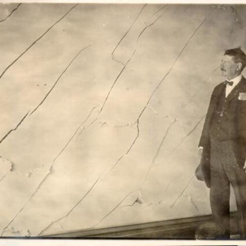 [Man standing before a cracked wall damaged by the 1906 earthquake and fire]