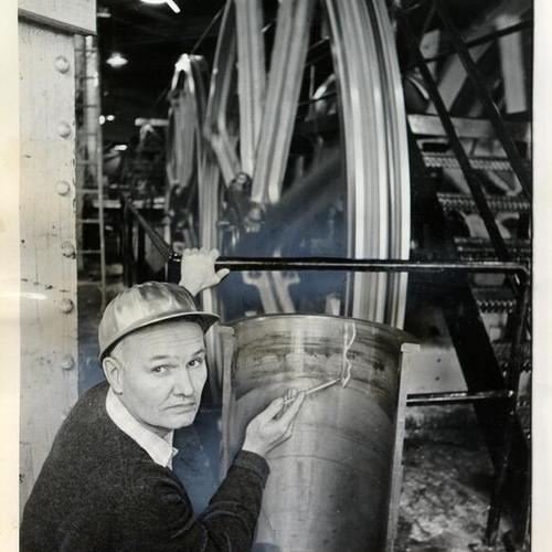 [Otto Heyer pointing to a crack in a piece of machinery at a cable car powerhouse]