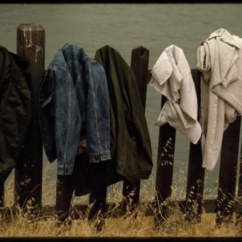 Jackets hung on a wooden fence by the water