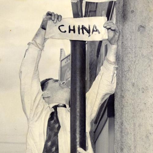 [Unidentified man placing a paper sign of China over Japan street]