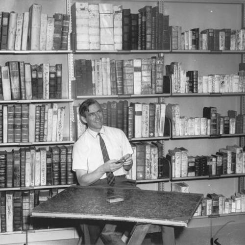 [Richard Dillon, Sutro Library curator, holding the smallest and largest of books in the collection at the Gleeson Memorial Library of University of San Francisco]