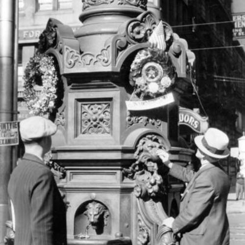 [Two men laying memorial wreaths on Lotta's Fountain]