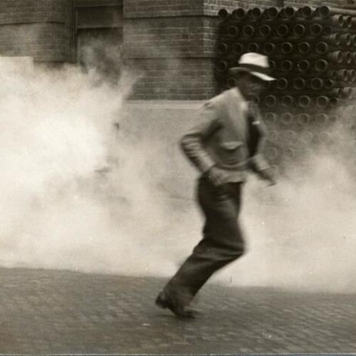 [Unidentified man running from tear gas during clash between striking longshoremen and police]