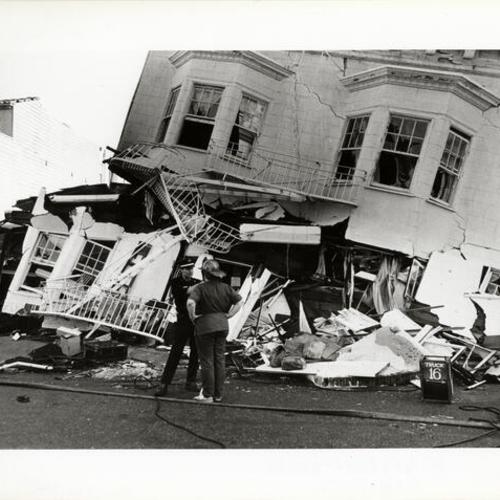 [Two firemen standing in front of a building destroyed in the October 17, 1989 Loma Prieta earthquake]