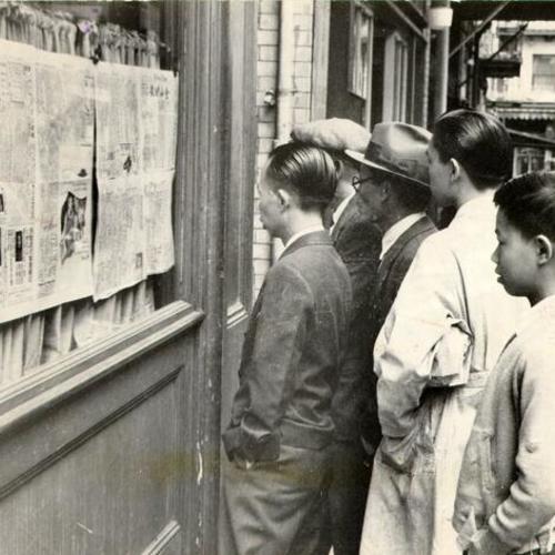 [Group of men standing outside of a Chinese newspaper office reading the latest news in Chinatown]