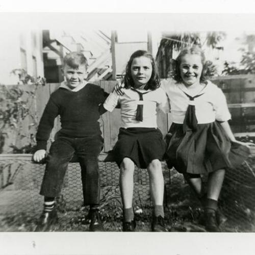 [Peter, Marilyn and classmate sitting on fence in backyard of home on Bush Street in 1943]