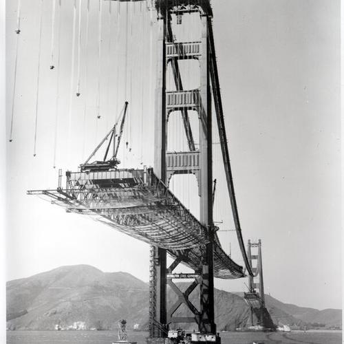 [Partly constructed Golden Gate Bridge deck hung from steel cables]