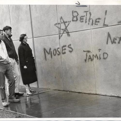 [Three students looking at anti-semitic graffiti on wall of Cloud Hall at City College of San Francisco]