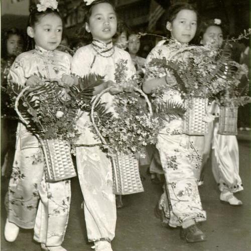[Four young girls carrying flowers in a parade in honor for Madame Chiang Kai-Shek]