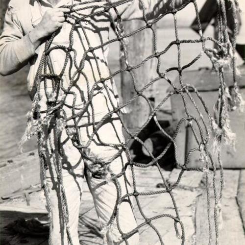 [Carpenter B. J. Gunderson holding a piece of a torn safety net after an accident occurred in which ten construction workers on the Golden Gate Bridge were killed when a work platform collapsed]