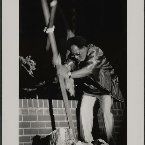 Reverend Cecil Williams breaking a rock (symbolic of crack cocaine) with wooden cross on Easter