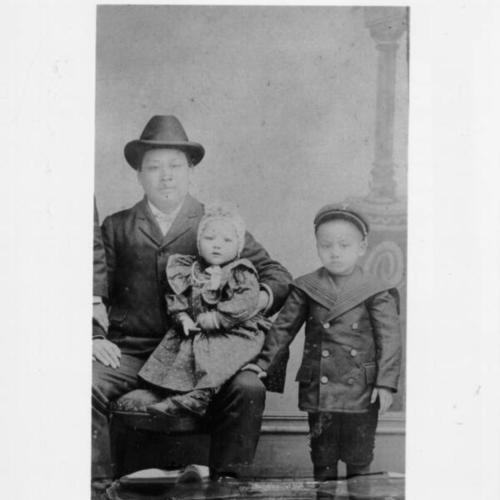 [Lew Hing, with his daughter Rose Lew Moon on his knee, and one of his son's standing at his side]