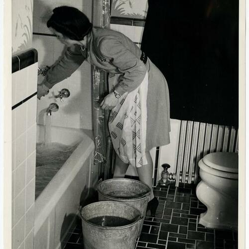 Person demonstrating what to do in the event of air raids sirens by filling buckets and bathtubs with water