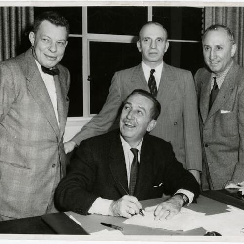[Walt Disney (seated), Robert E. Kintner, Sidney M. Markley, and Roy O. Disney]