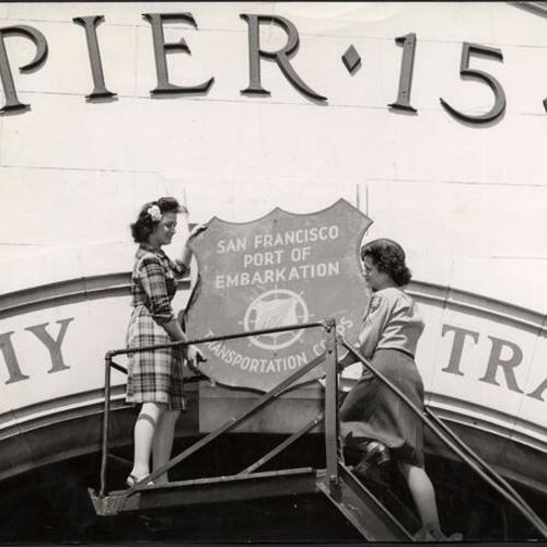 [Bonita Pittack and Ruth Butler take the Port of Embarkation shield off of Pier 15]