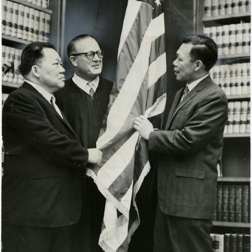 [Samuel Wong, Mann Wong and Judge Oliver J. Carter standing before the American flag]