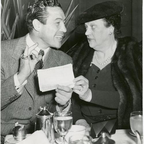 [Max Baer and Alma de Bretteville Spreckels at luncheon hold paper titled Make a service man happy]