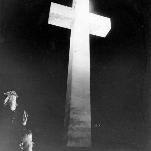 [Mother and child kneeling before cross on Mount Davidson]