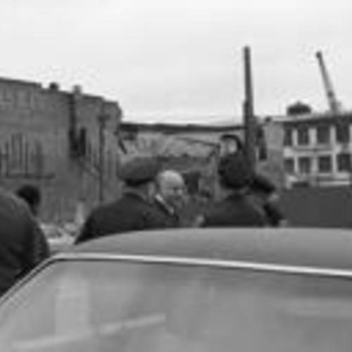 [Mayor Joseph Alioto talks with uniformed men, demolished building in background,