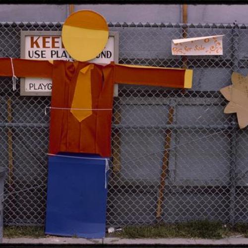 Cardboard cut out of person attached to fence