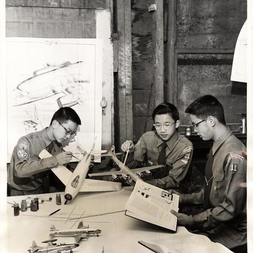 [Air Explorer Scouts Balfour Chinn, Russell Woo and Melvin Lee working with charts and models of planes they will use in their 'Model Air Field' booth at the 1956 Boy Scout Exposition]