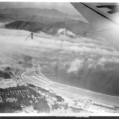 [Aerial view of fog over Golden Gate Bridge photographed from passing airplane]