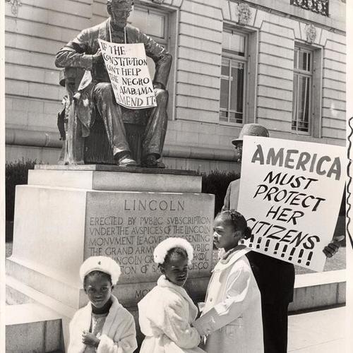 [Man and three girls protesting against racial discrimination next to statue of Abraham Lincoln]