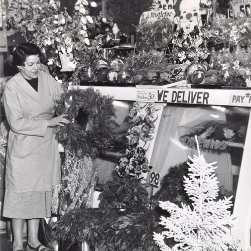 [Marian Abrahamson holding a Christmas wreath at a flower stand in the Crystal Palace Market]