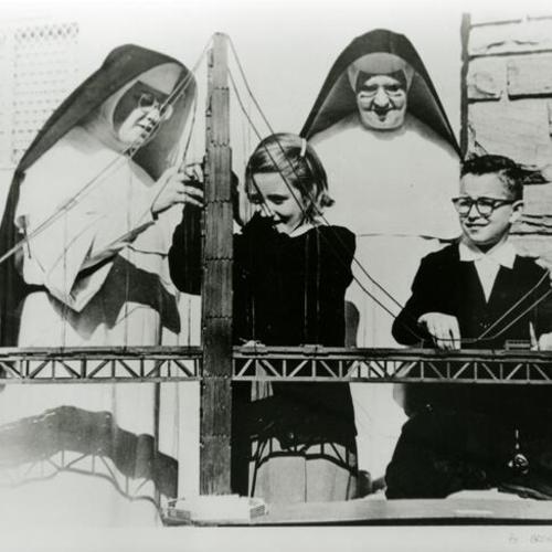[Two Dominican Sisters and two children next to model of Golden Gate Bridge]