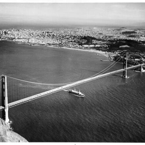 [Aerial view of the Golden Gate Bridge from the Marin County side, showing a ship passing underneath the bridge and San Francisco in the distance]