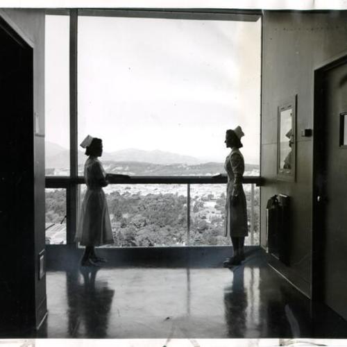 [Nurses Hideko Wada and Anita Miller looking out a window in the obstetrical ward on the fifteenth floor of the Herbert C. Moffitt Hospital at U. C. Medical Center]