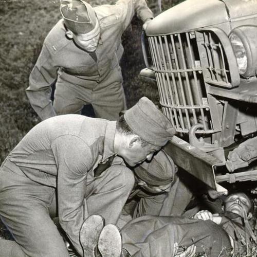 [Private Edward Wax being removed from beneath an automobile during Red Cross first aid training at the Presidio]