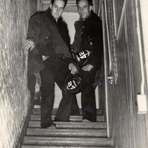 [Two firemen standing on a narrow stairway of a fire house in 1941]