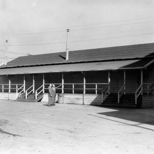 [Two unidentified men looking at a temporary wooden building at Portola Junior High School]