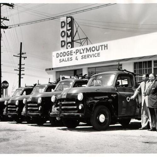 [Victor Martin and Frank Sherman of S & M Motors posing with four new Dodge trucks]
